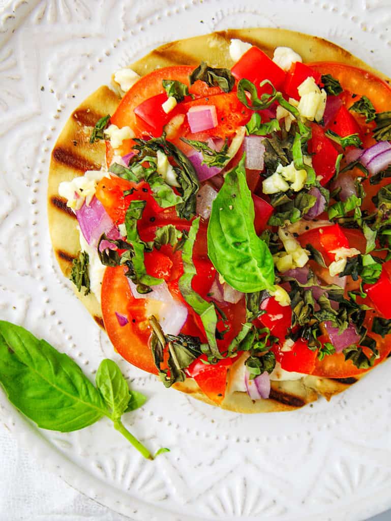 healthy pita pizza with goat cheese and tomatoes, served on a white plate, garnished with basil