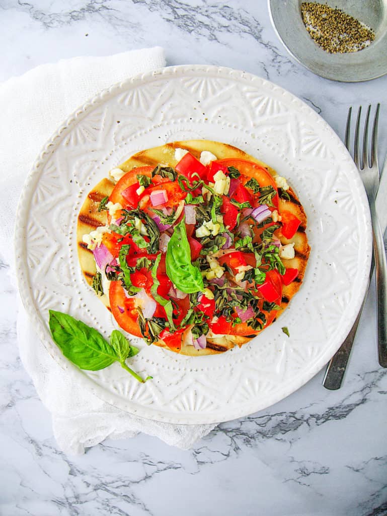 healthy pita pizza with goat cheese and tomatoes, served on a white plate, garnished with basil