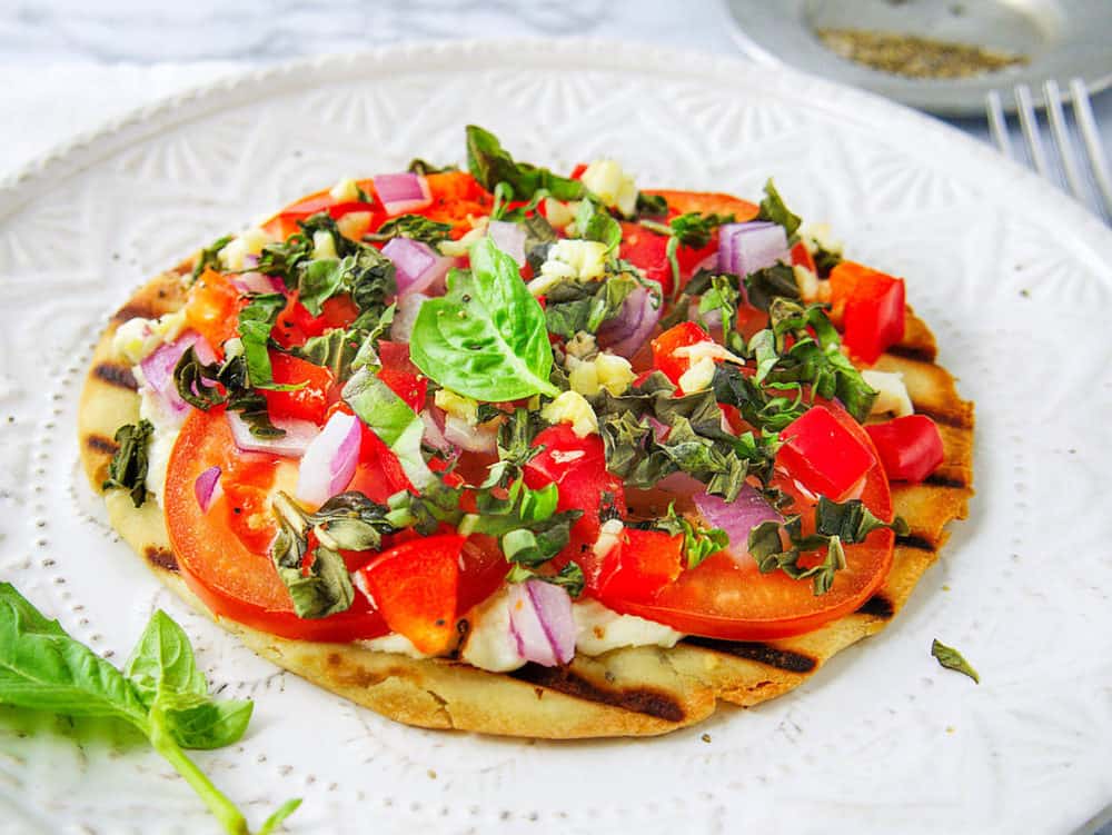 healthy pita pizza with goat cheese and tomatoes, served on a white plate, garnished with basil