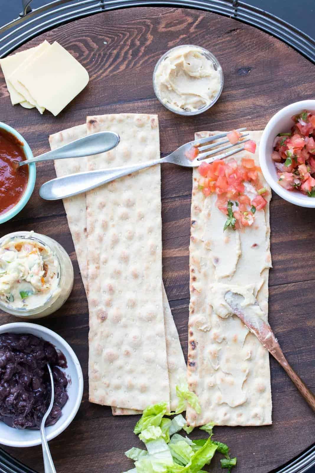 These vegan pinwheels are the perfect snack! Super kid friendly, versatile and easy enough the littles can make them too! #ad #vegansnacks #kidsrecipes Knife spreading cream cheese and fork spreading salsa on slices of lavash bread