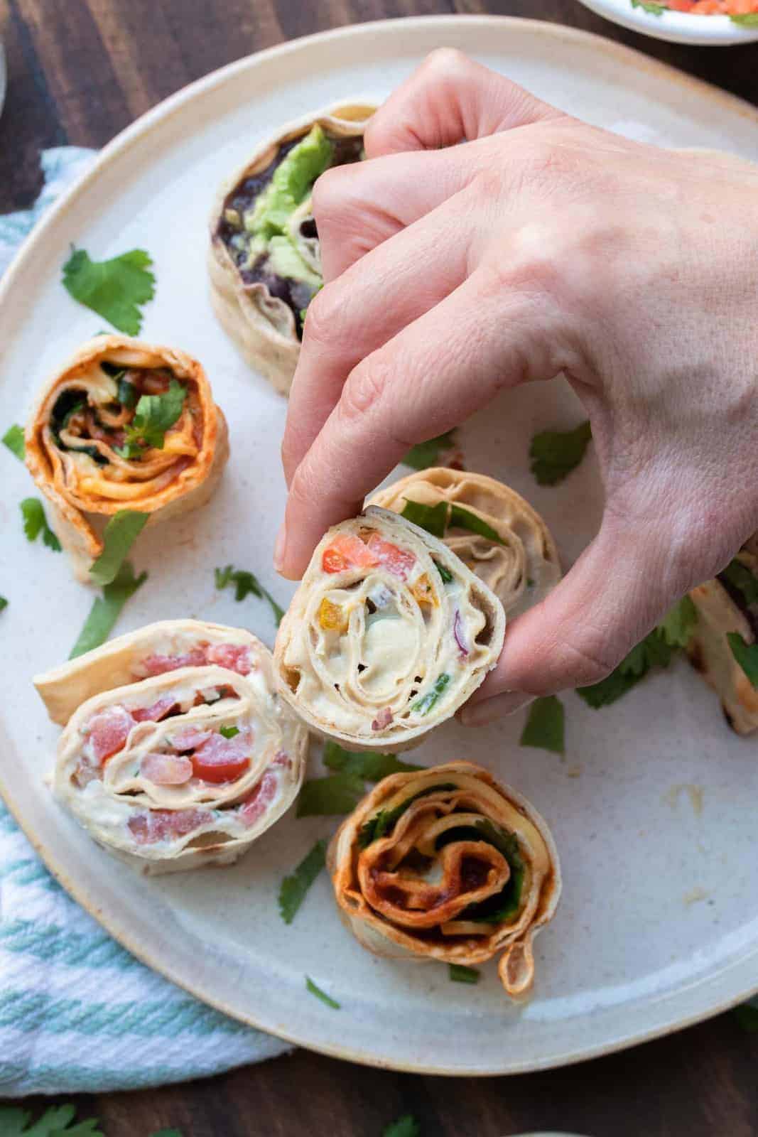 These vegan pinwheels are the perfect snack! Super kid friendly, versatile and easy enough the littles can make them too! #ad #vegansnacks #kidsrecipes Hand grabbing a pinwheel sandwich filled with veggies and cream cheese