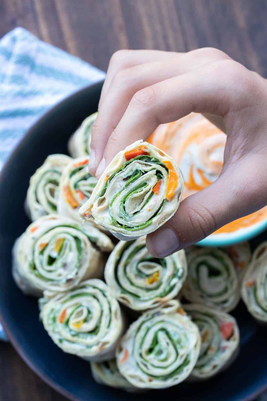 These vegan pinwheels are the perfect snack! Super kid friendly, versatile and easy enough the littles can make them too! #ad #vegansnacks #kidsrecipes Hand picking up a lettuce, salsa and cream cheese pinwheel sandwich