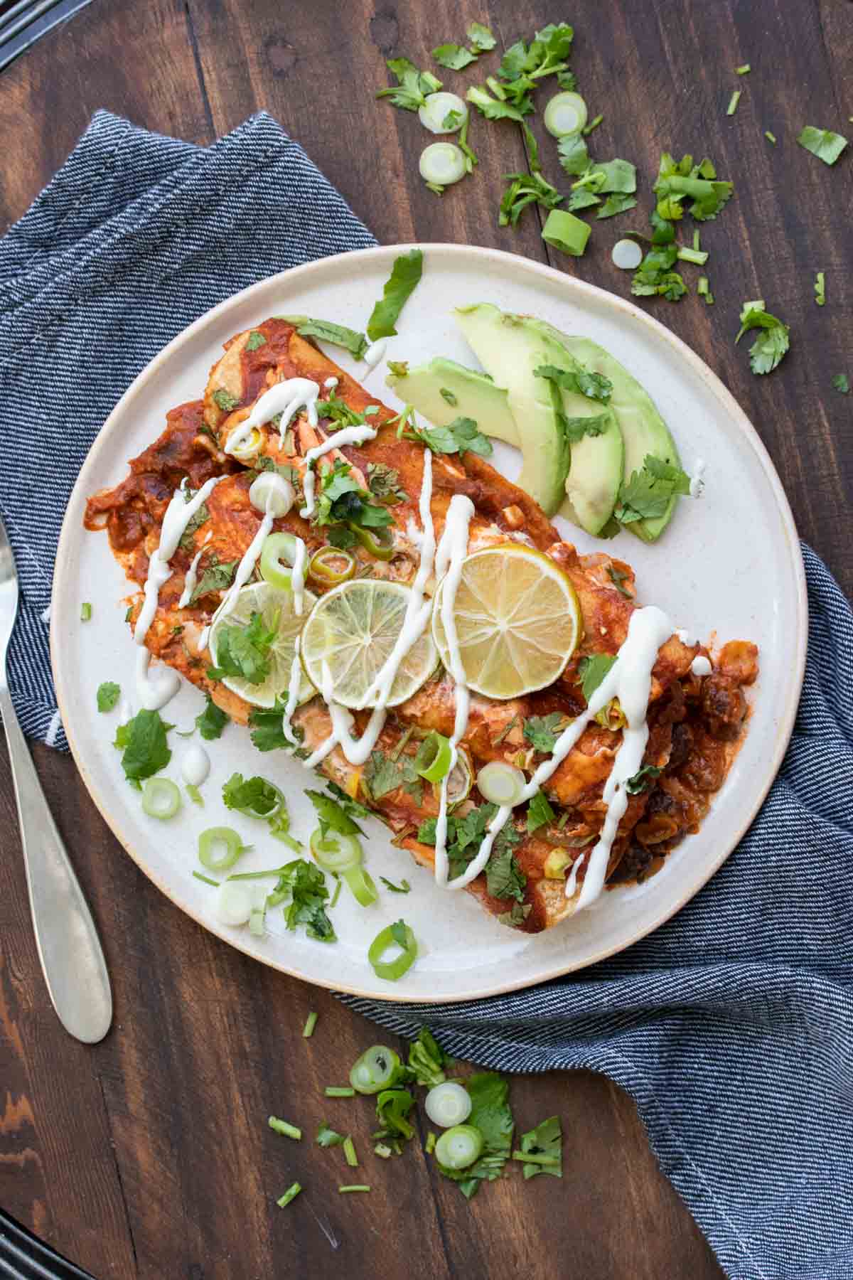 Vegan black bean enchiladas packed with veggies and an incredible flavor. They're super simple to put together and make a meal the whole family will love! #veganmexicanrecipes #healthyvegandinner White plate with two red sauce enchiladas drizzled with sour cream