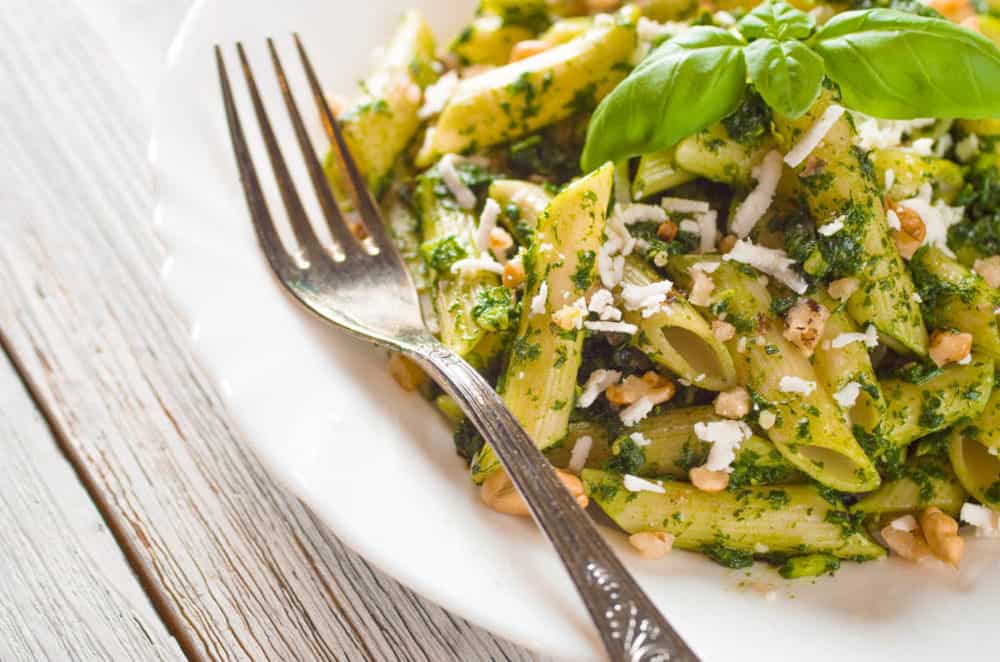 closeup of Vegetarian Pesto with Whole Wheat Pasta, topped with fresh basil, served on a white plate with a fork - 30 minute vegetarian meals