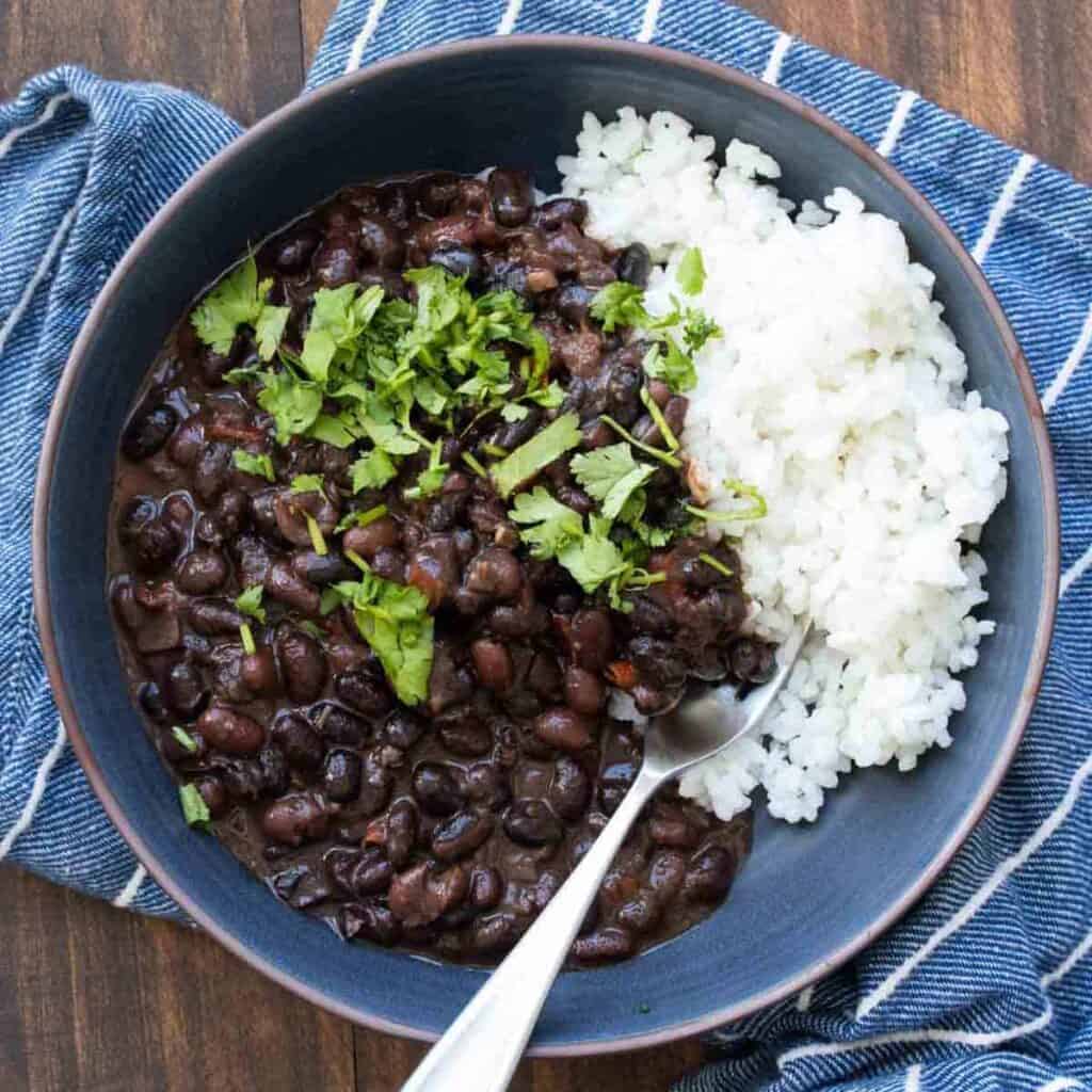 A blue bowl on a blue striped towel that is filled with black beans and white rice with cilantro on top.