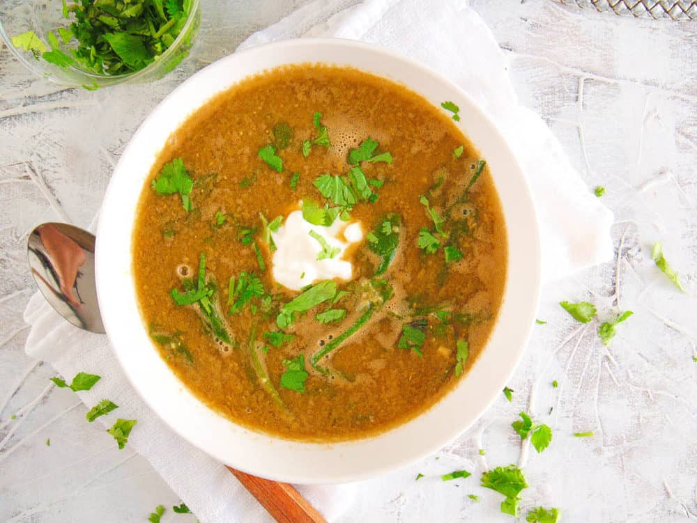 lebanese lentil soup with spinach, served in a white bowl with cilantro on top