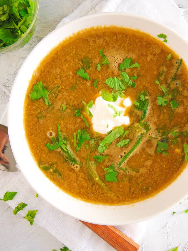 lebanese lentil soup with spinach, served in a white bowl with cilantro on top