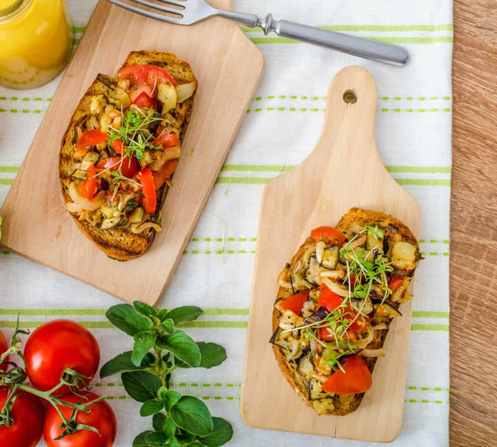 Caprese Bruschetta with vegetables, served on a wooden cutting board with a white and green napkin in the background