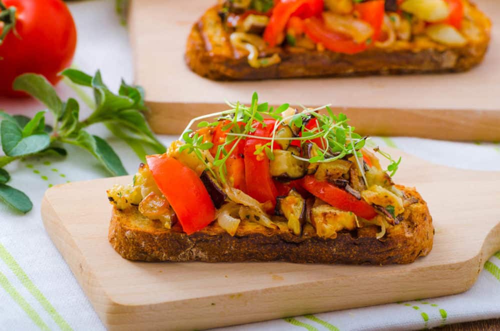 Caprese Bruschetta with vegetables, served on a wooden cutting board with a white and green napkin in the background