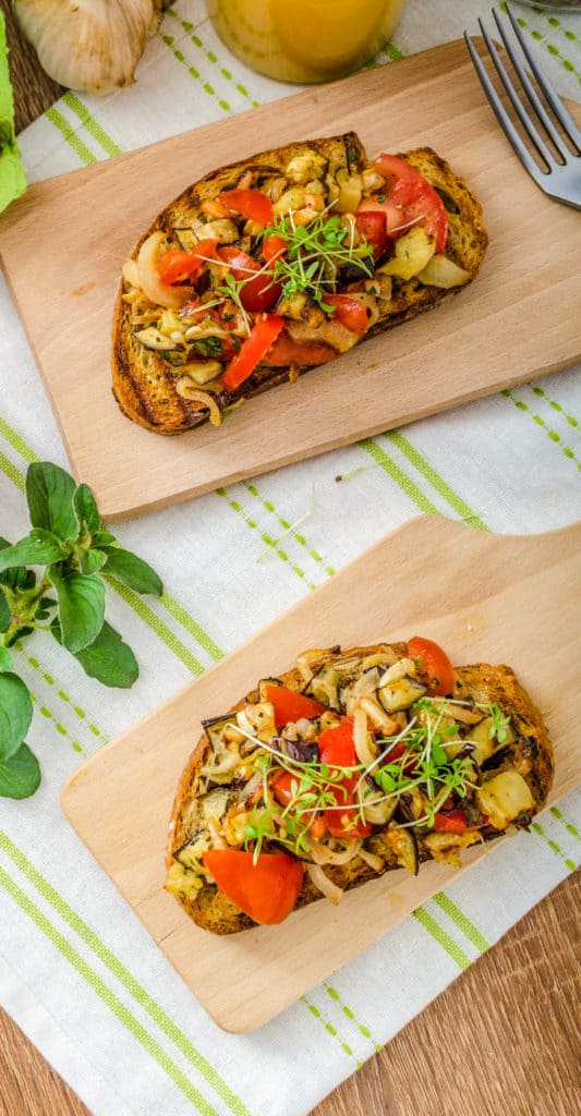 Caprese Bruschetta with vegetables, served on a wooden cutting board with a white and green napkin in the background