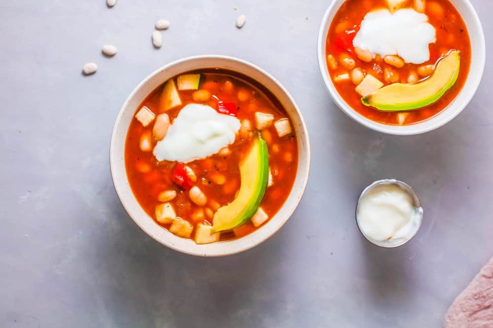 vegan white bean soup served with avocado and greek yogurt in a white bowl