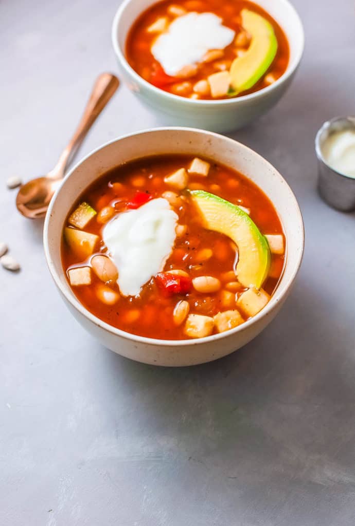 vegan white bean soup served with avocado and greek yogurt in a white bowl