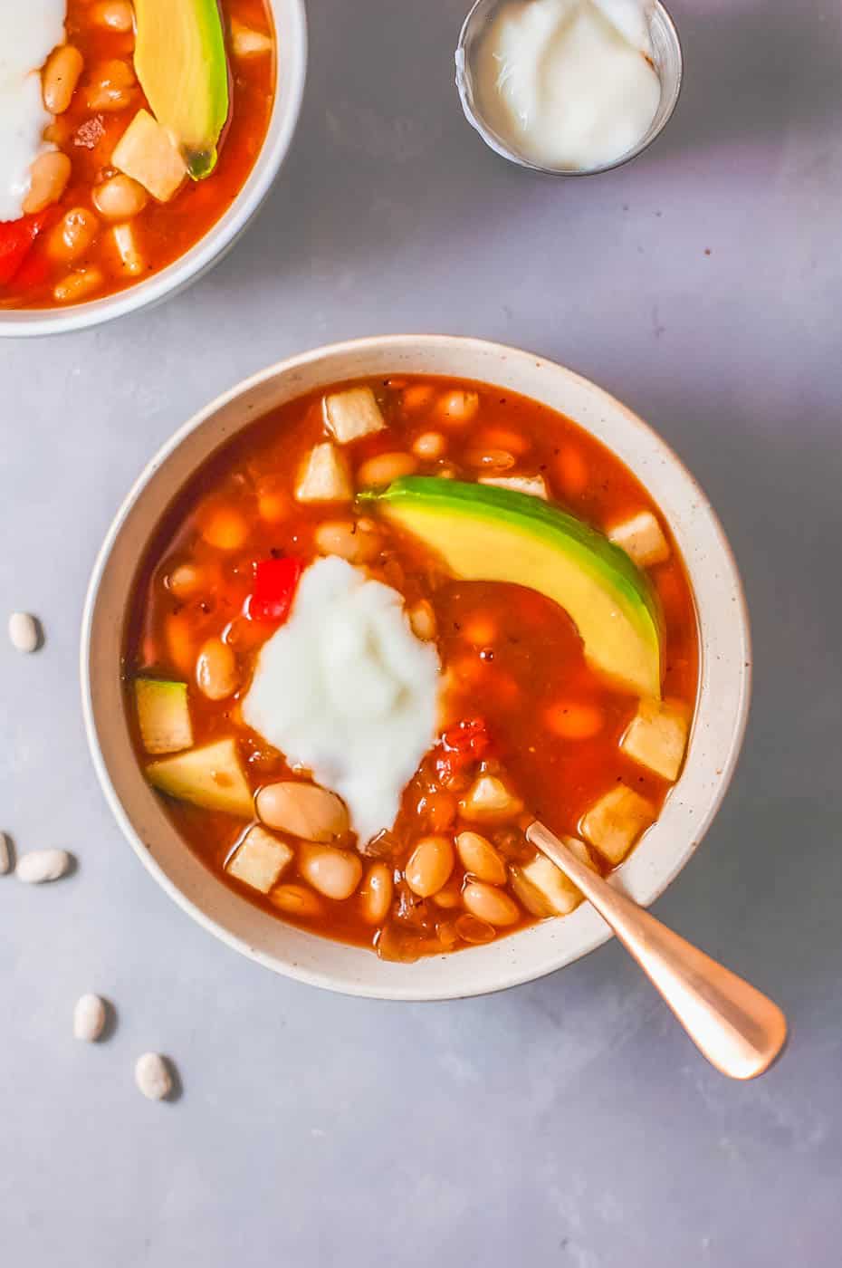 vegan white bean soup served with avocado and greek yogurt in a white bowl