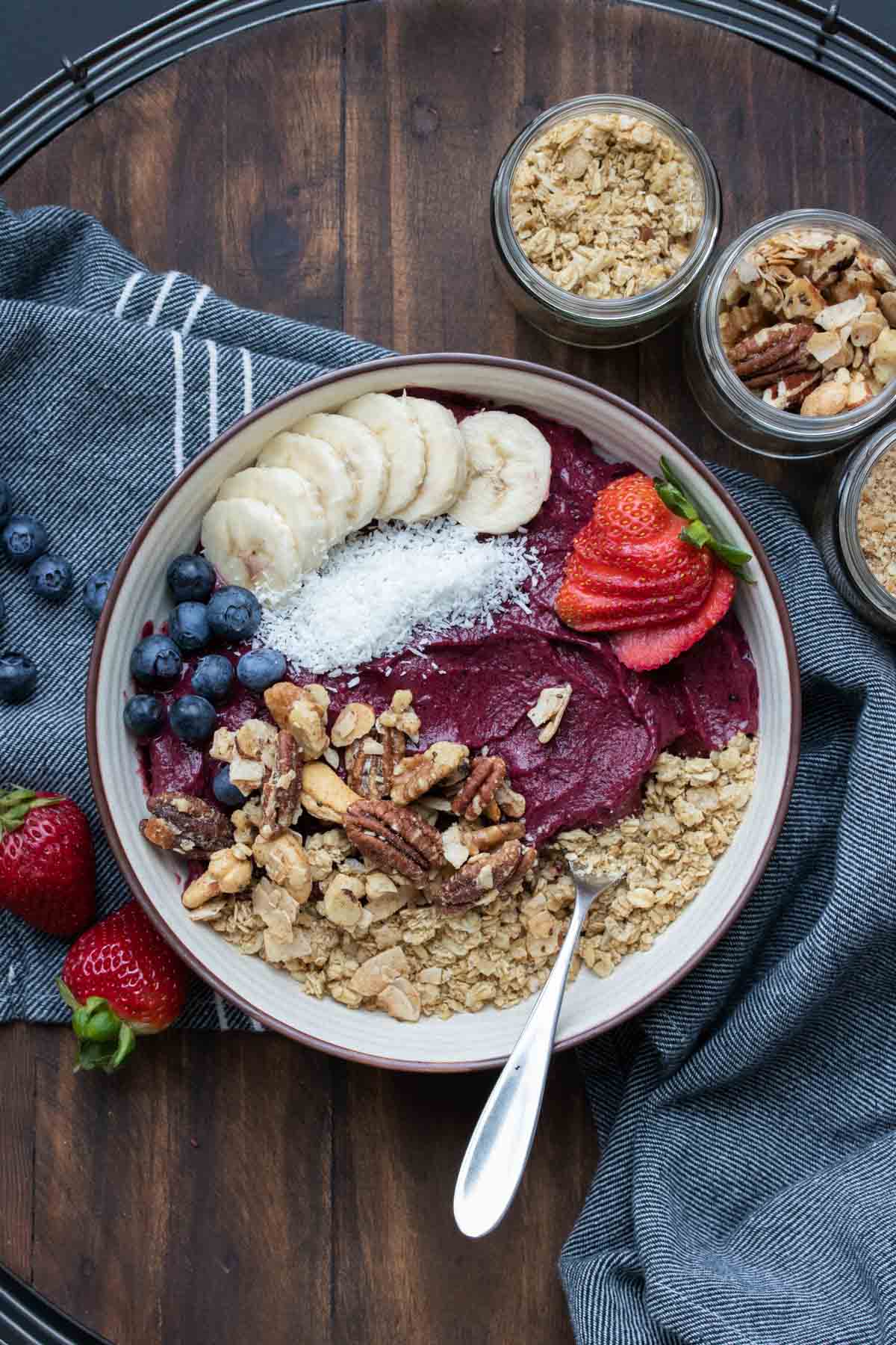 A vegan smoothie bowl in a cream bowl topped with fruit and nuts.