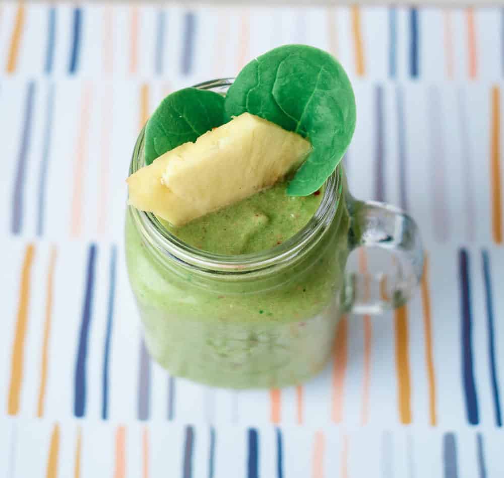 smoothie served in a glass mason jar, topped with pineapple and spinach leaves