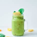 fruit and vegetable smoothie, served in a glass mason jar, topped with pineapple and spinach leaves