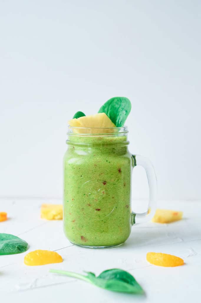 fruit and vegetable smoothie, served in a glass mason jar, topped with pineapple and spinach leaves