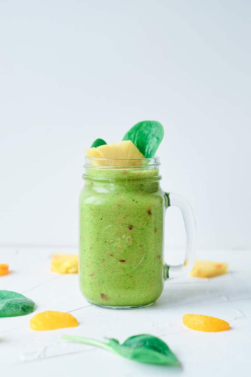 fruit and vegetable smoothie, served in a glass mason jar, topped with pineapple and spinach leaves