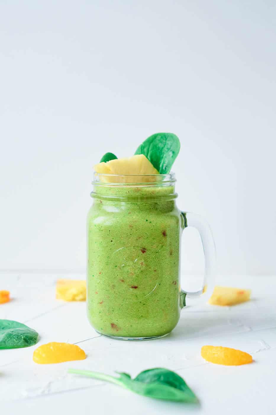 fruit and vegetable smoothie, served in a glass mason jar, topped with pineapple and spinach leaves