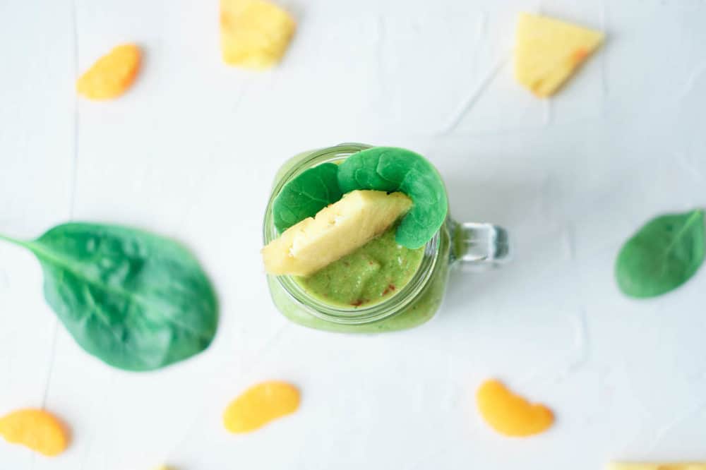 top view of fruit and vegetable smoothie, served in a glass mason jar, topped with pineapple and spinach leaves