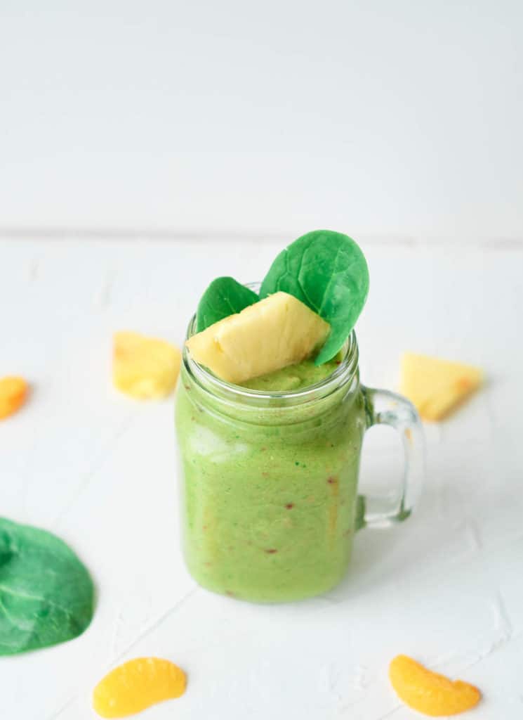 fruit and vegetable smoothie, served in a glass mason jar, topped with pineapple and spinach leaves