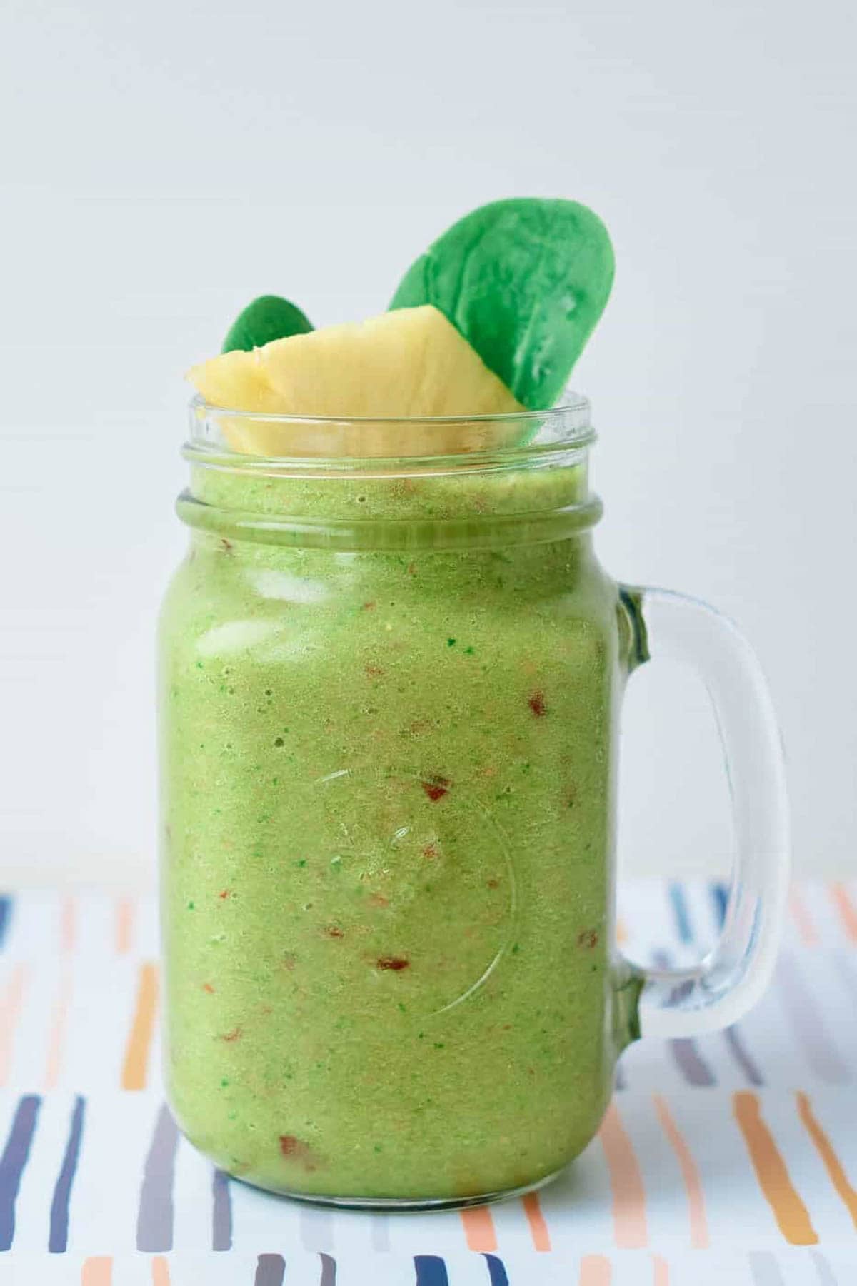 Fruit and vegetable smoothie recipe served in a glass mason jar, garnished with spinach leaves and pineapple chunks.