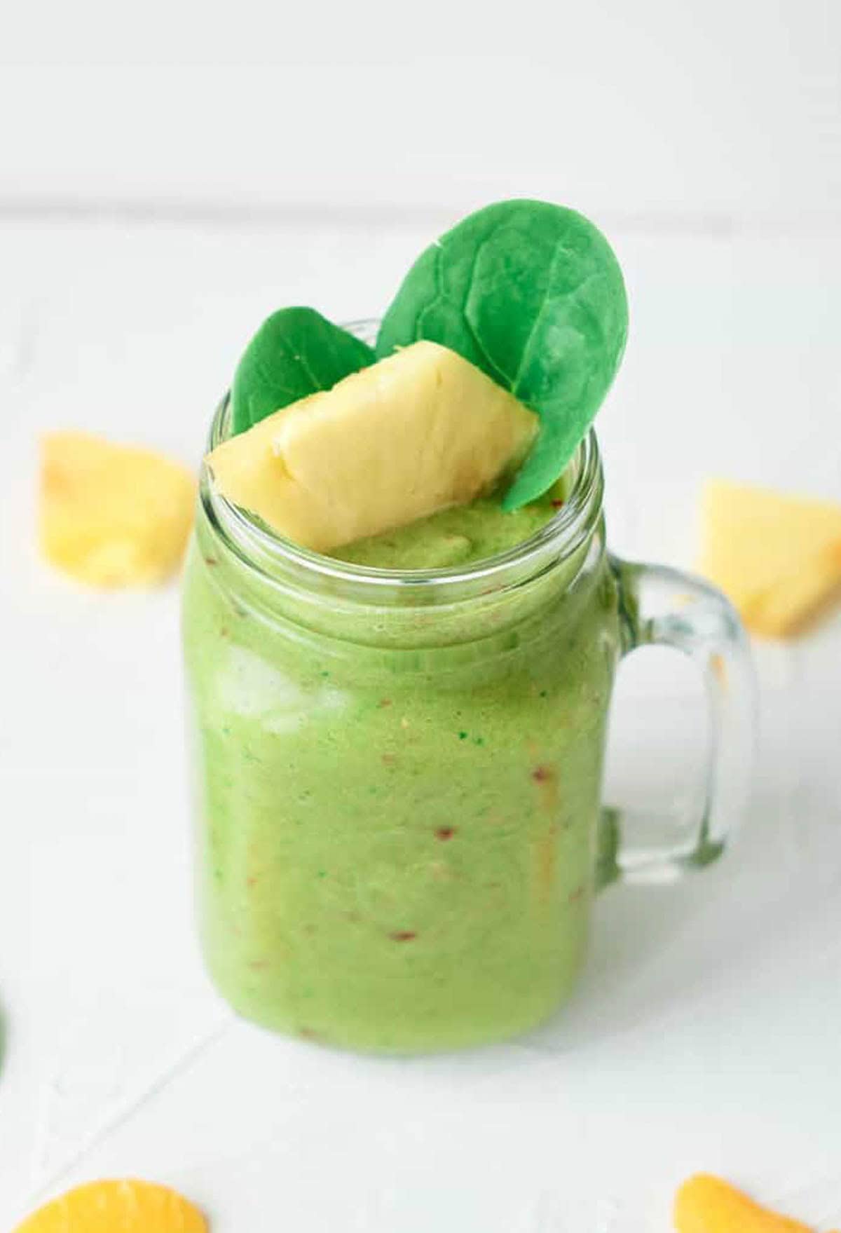 Veggie fruit smoothie served in a glass mason jar, garnished with spinach leaves and pineapple chunks.