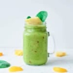 Fruit and veggie smoothie served in a glass mason jar, garnished with spinach leaves and pineapple chunks.