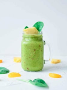 Fruit and veggie smoothie served in a glass mason jar, garnished with spinach leaves and pineapple chunks.