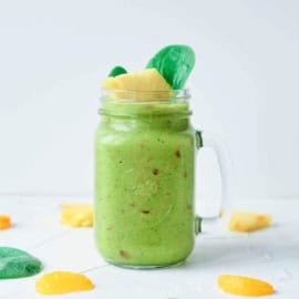 Fruit and veggie smoothie served in a glass mason jar, garnished with spinach leaves and pineapple chunks.