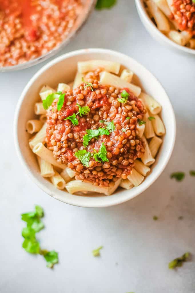 vegan bolognese with lentils, served over pasta in a white bowl