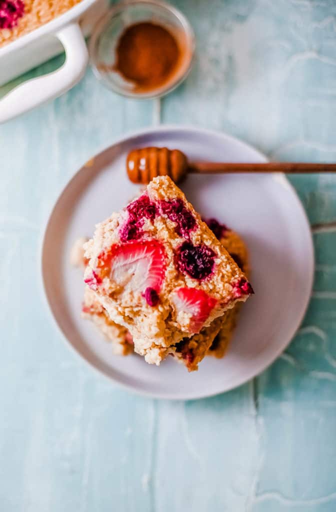 cut squares of vegan baked oatmeal topped with berries, served on a white plate