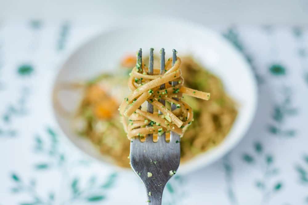 fork of vegetarian pesto pasta with spinach and herbs, served on a white plate