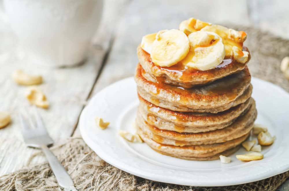 Healthy Pancakes Made with Oats and Sprouted Wheat topped with bananas and served on a white plate