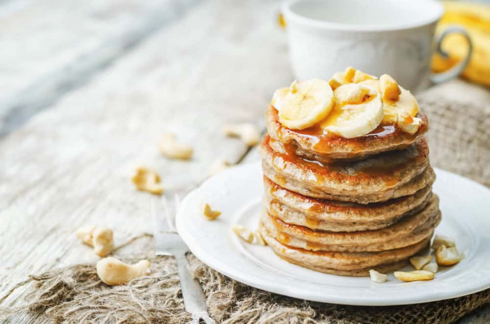 Pancakes Made with Oats and Sprouted Wheat topped with bananas and served on a white plate
