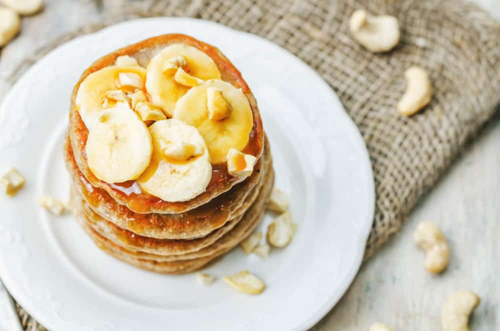 Healthy Pancakes Made with Oats and Sprouted Wheat topped with bananas and served on a white plate