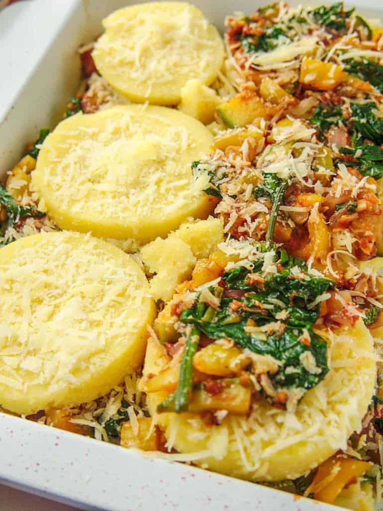 Veggies and polenta slices layered in a baking dish.