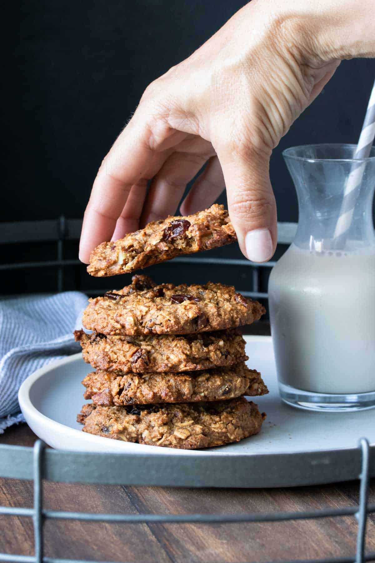 Hand grabbing the top oatmeal raisin cookie from a stack on a plate.