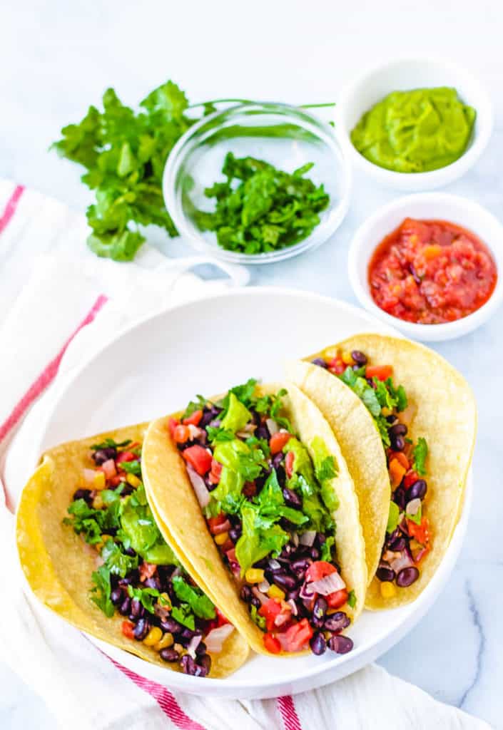 vegan tacos with black beans, avocado, veggies, and cilantro, served on a white plate