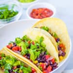 vegan tacos with black beans, avocado, veggies, and cilantro, served on a white plate