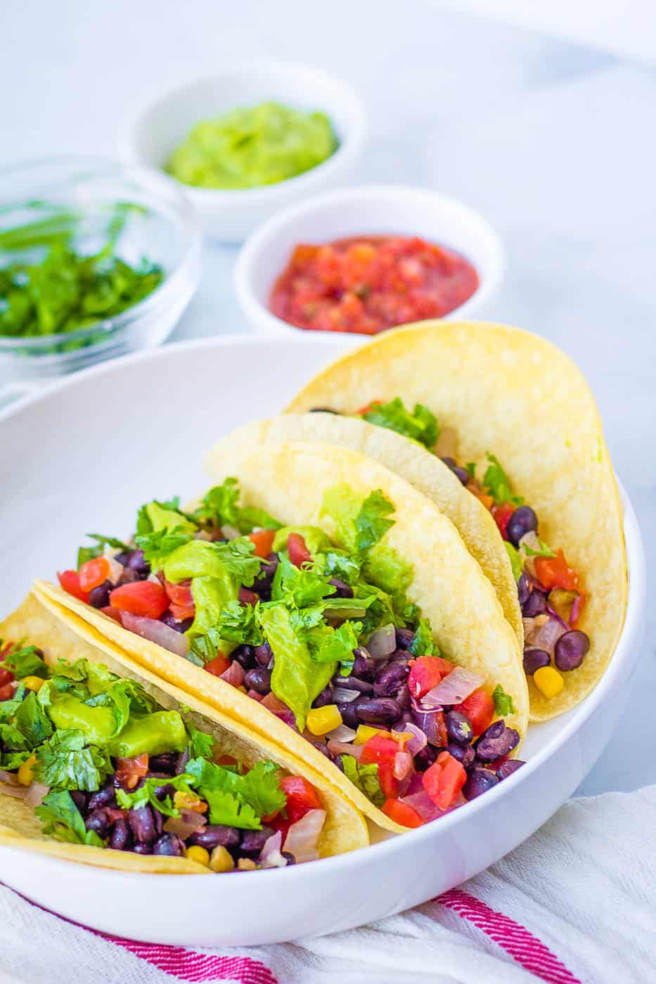 vegan tacos with black beans, avocado, veggies, and cilantro, served on a white plate