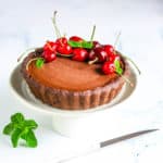 Chocolate Ganache Tart with cherries on top, served on a white plate