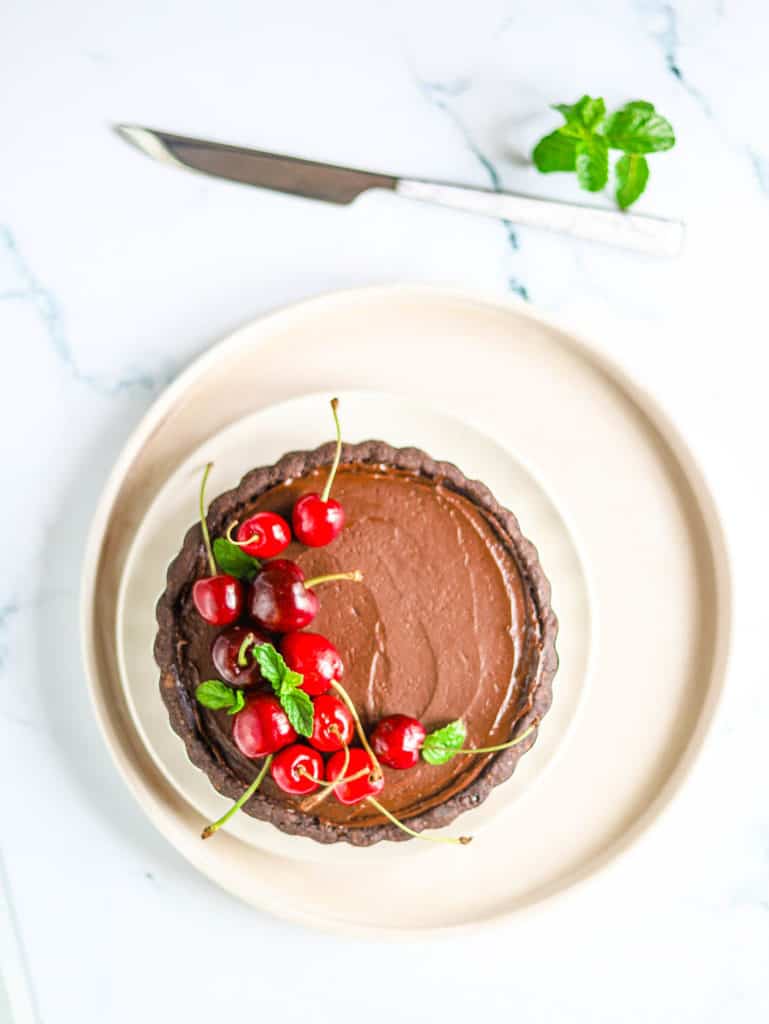 Chocolate Ganache Tart with cherries on top, served on a white plate