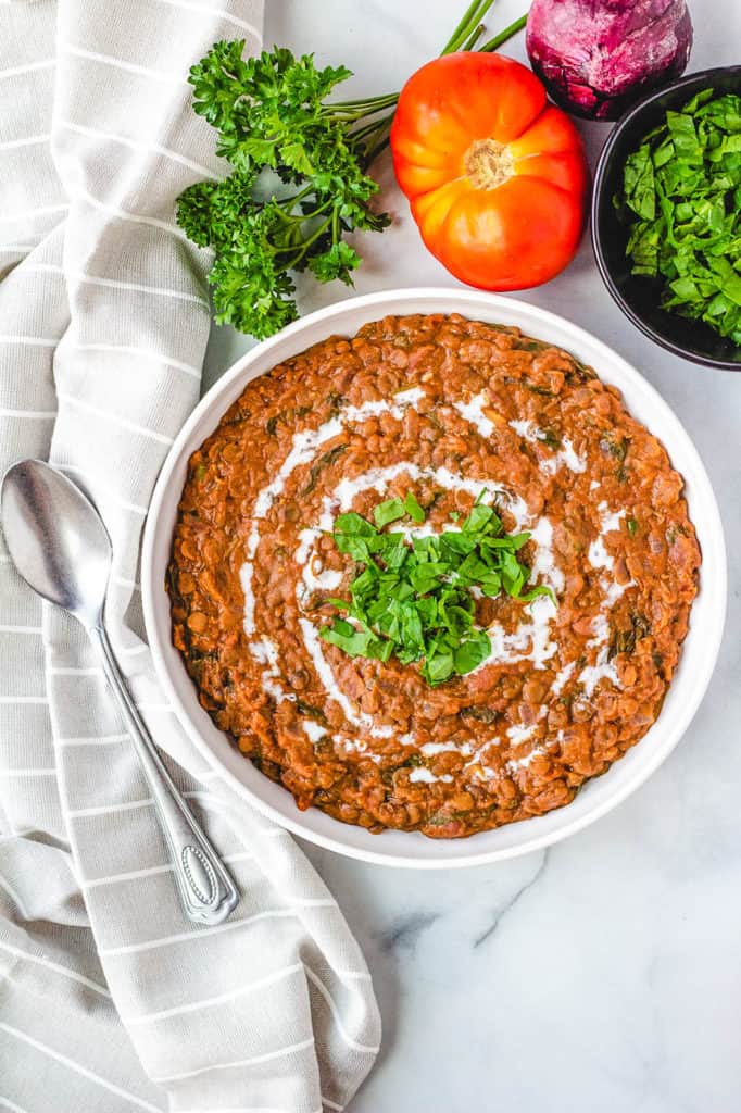 top view of instant pot vegan dal makhani recipe, served in a white bowl with fresh herbs on top