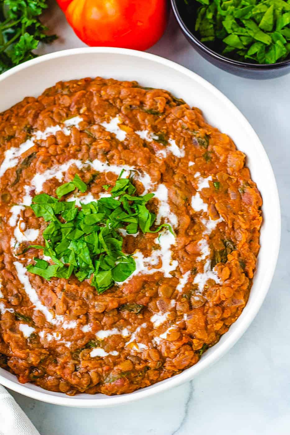 top view of instant pot vegan dal makhani recipe, served in a white bowl with fresh herbs on top