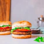 falafel burgers pictured against a marble background, topped with tomatoes and lettuce and a feta sauce