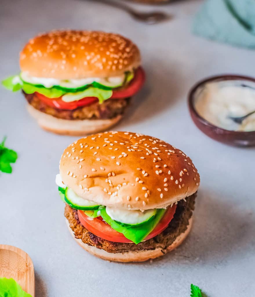 falafel burgers pictured against a marble background, topped with tomatoes and lettuce and a feta sauce