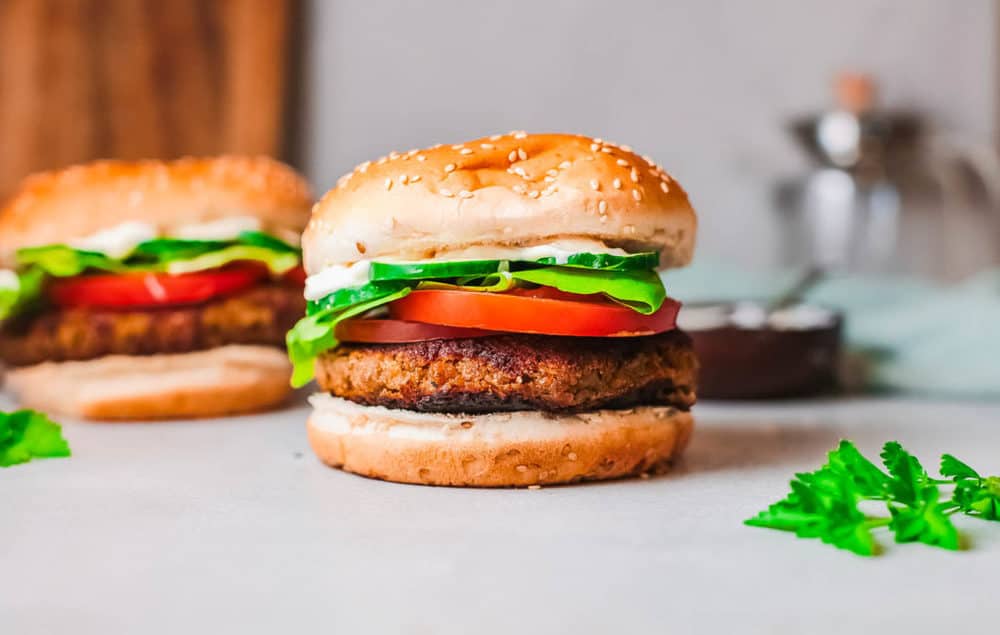 falafel burgers pictured against a marble background, topped with tomatoes and lettuce and a feta sauce