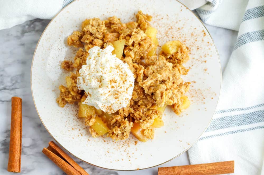 gluten free apple crisp served on a white plate topped with whipped cream