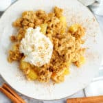gluten free apple crisp served on a white plate topped with whipped cream